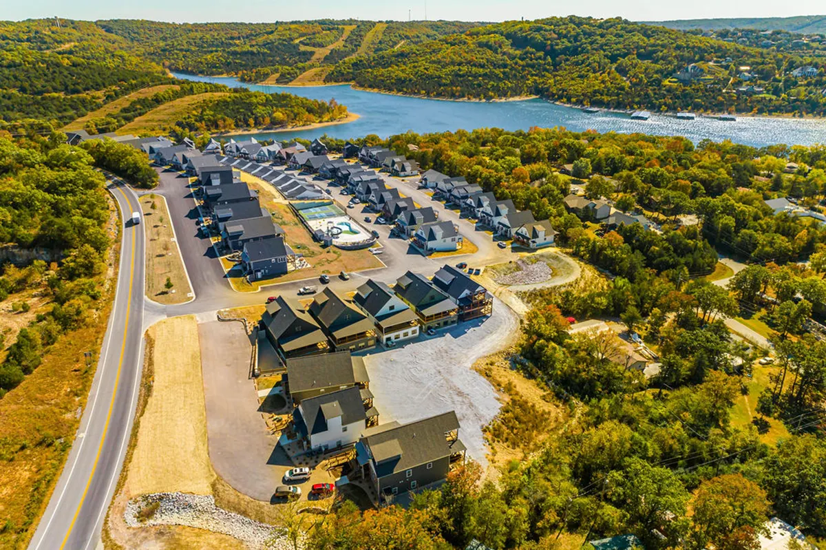 Overlooking a swimming pool, winding road, and glimmering lake against a backdrop of residential buildings, this exterior shot captures the scenic beauty and recreational abundance of the community. The landscape hints at boating, hiking, and relaxation all within reach.