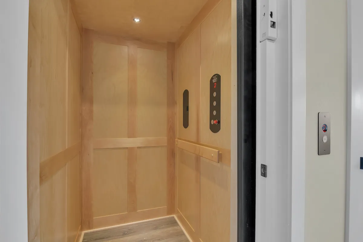 A detail view of an elevator interior with wooden paneling and smooth flooring, focusing on the control buttons for easy operation. The design is practical, modern, and ADA-friendly, emphasizing accessibility throughout the home.