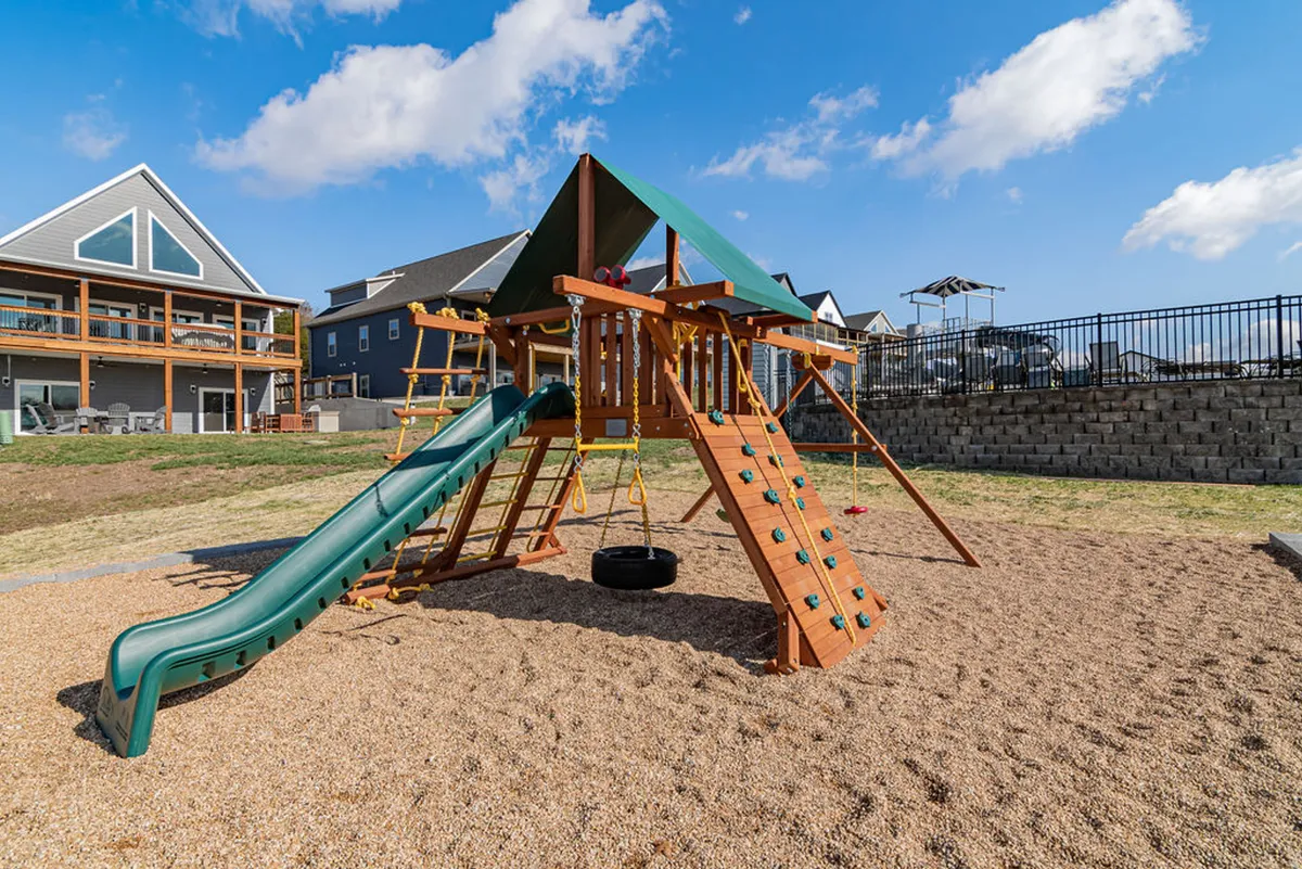 A cheerful outdoor playground with a slide, swing, and sandbox area, where children are seen playing while parents relax nearby. The setting is open, safe, and easily accessible, ideal for inclusive family gatherings.