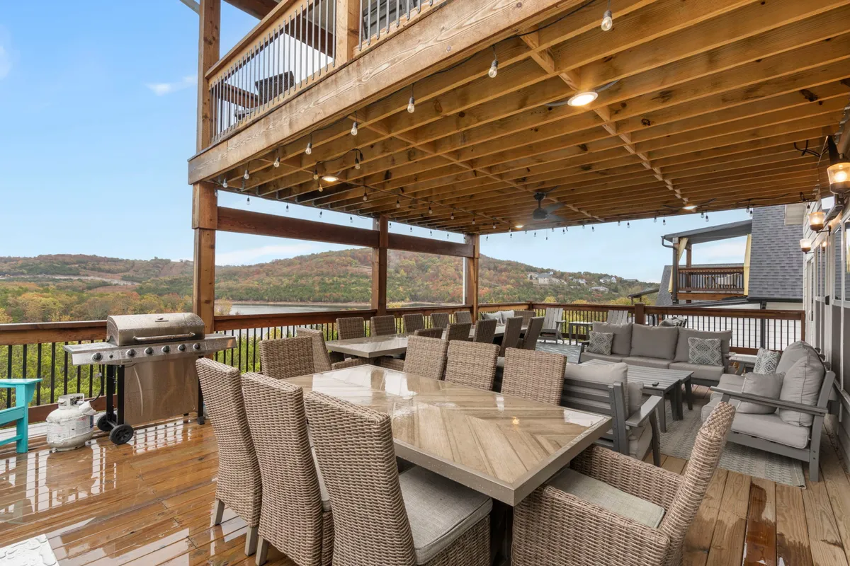 An expansive exterior dining area featuring a large table, comfortable seating, and a prominent grill setup, all overlooking a panoramic view of rolling hills. The scene is bathed in natural light, ideal for group gatherings and outdoor feasts.