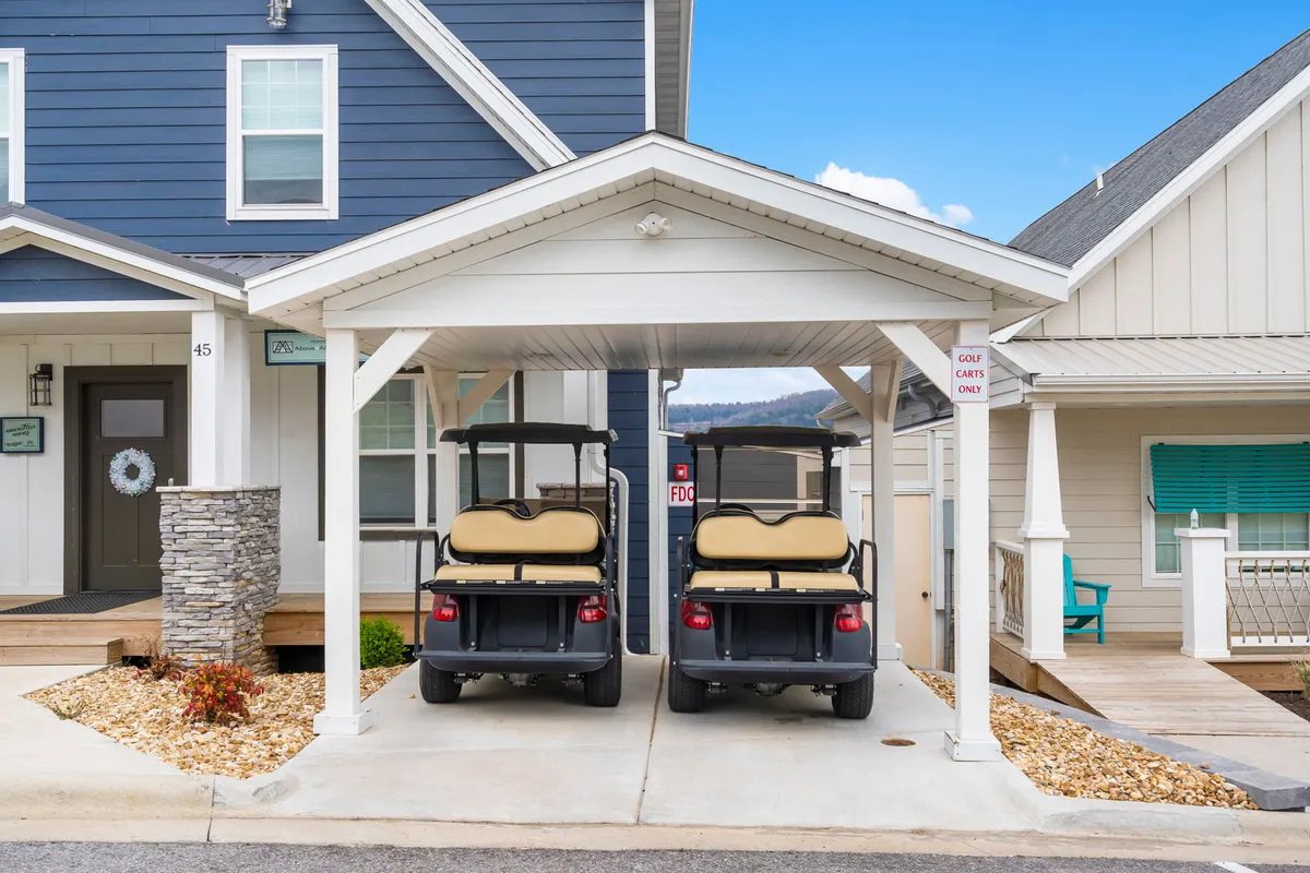 A welcoming exterior shot featuring two golf carts parked near a home's front entrance with stone columns and an overhanging roof. The scene feels casual and accessible, emphasizing the ease of getting around the resort and down to the water. The image suggests a leisurely lifestyle and convenient, fun exploration for all ages.