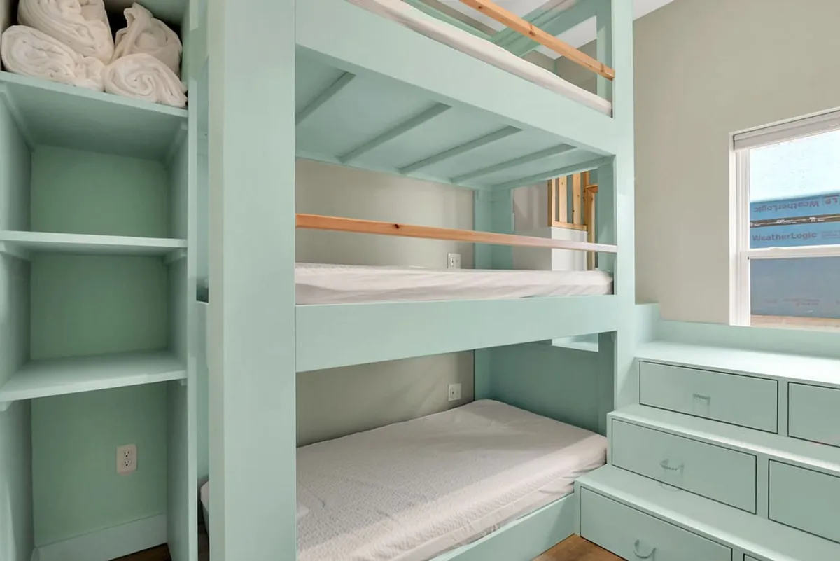A cheerful and cozy bunk room designed for kids, featuring a sturdy bunk bed, built-in storage drawers, and shelves neatly stocked with rolled towels. The space is brightly lit, playful, and designed for both sleep and creative play.