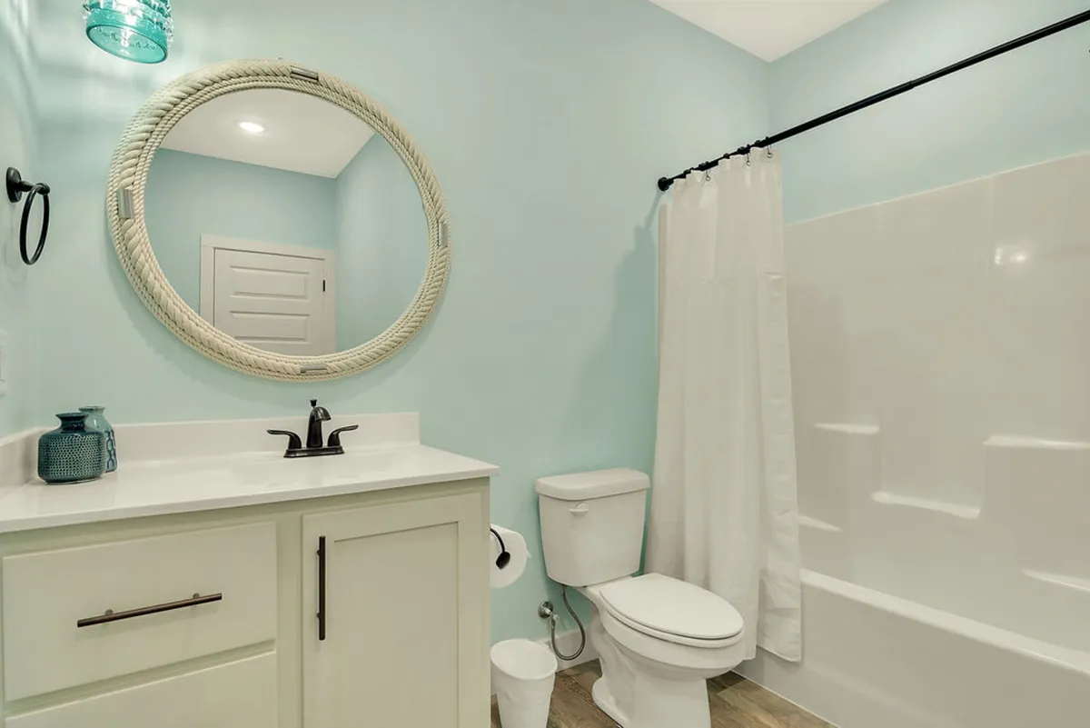 A bright, spa-inspired bathroom featuring a large round mirror, modern sink, and a colorful light fixture. The space is light and airy, ideal for personal grooming and relaxation.