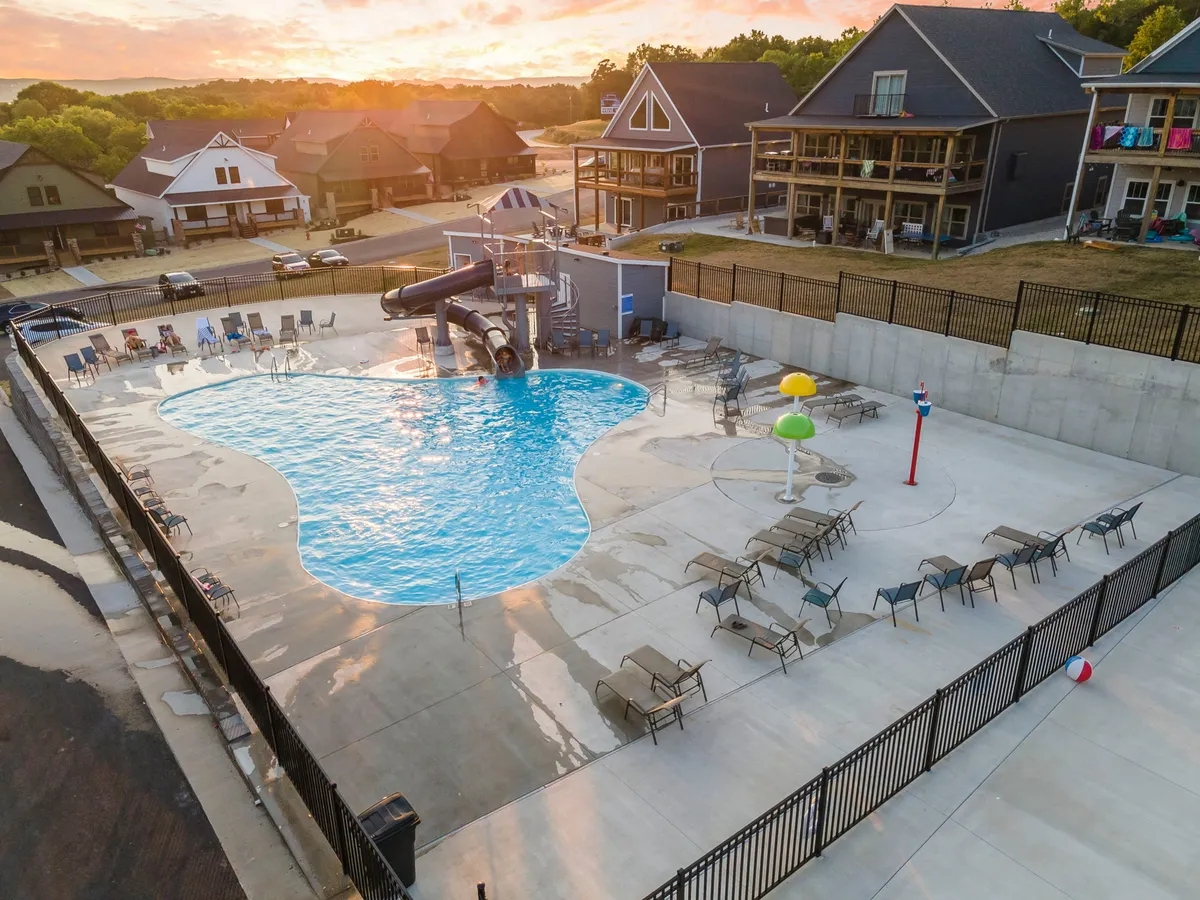 A vibrant pool scene with a water slide, lounge chairs, and colorful water features. Families and children are enjoying swimming, sunbathing, and playful moments under a joyful sunset sky, emphasizing both fun and relaxation after a day out.