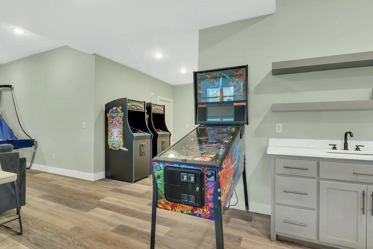A lively game room fitted with classic arcade machines, a pinball machine, and modern cabinetry. The space is designed for group gatherings, friendly competition, and all-ages fun, inviting guests to relive nostalgic moments or challenge each other to games.
