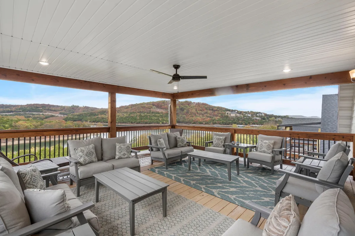 This exterior image presents a comfortable balcony seating area with decorative cushions, wooden beams, and an expansive view of the lake and hills beyond. Ideal for relaxing, toasting to sunsets, or capturing group photos with the scenic backdrop.