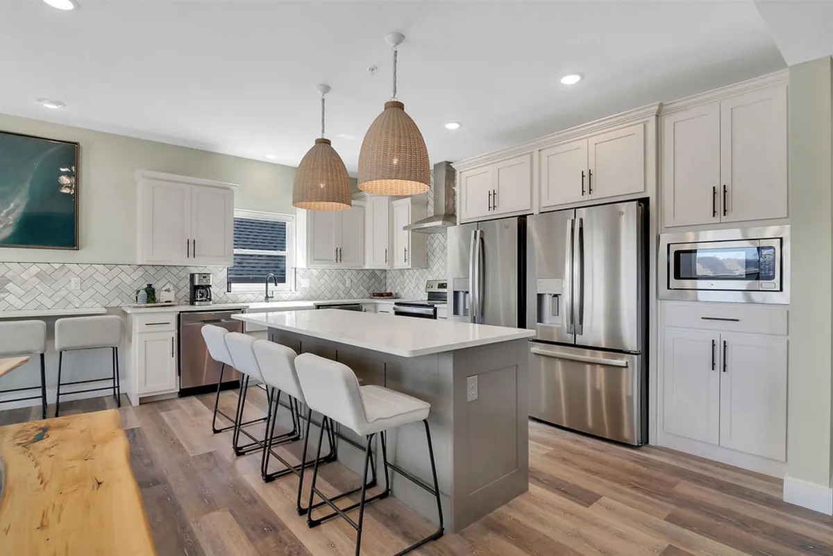 The image highlights a modern kitchen island with hanging pendant lights and stainless steel appliances in the background, suggesting a well-equipped culinary space. The area appears welcoming, ideal for communal cooking and hosting friends or family.